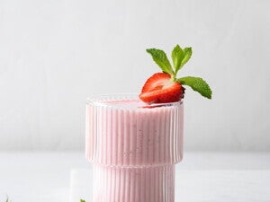 Batido Cremoso de Fresas Un vaso contiene batido de fresa y la fruta de decoración