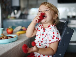 Niña pequeña en la cocina sonriendo y jugando con frambuesas en los dedos.