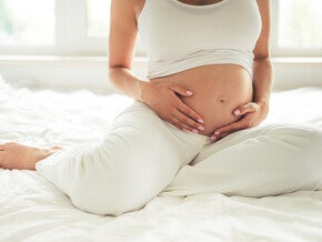 Mujer embarazada sentada en la cama sosteniendo su vientre.