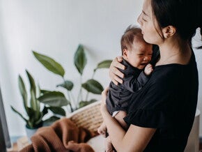 Mamá alzando y consolando a su bebé que llora sin razón aparente.
