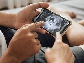 Close up de ultrasonido en un celular, manos de una pareja lo señalan