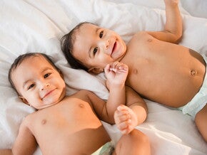 Bebés gemelos o mellizos acostados en una cama sonriendo.
