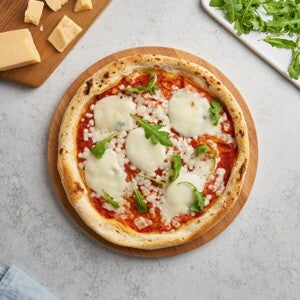 Pizza margarita en el centro con decoración de queso y albahaca alrededor