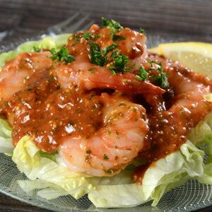 en un plato hay una base de ensalada y encima camarones con salsa
