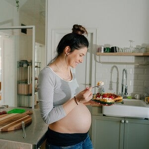 Mujer embarazada sonriendo en la cocina comiendo antojo dulce