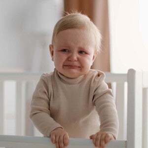 Bebé pequeño llorando dentro de su cuna, con expresión de incomodidad.