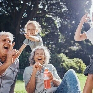 Personas adultas mayores y niños jugando al aire libre con burbujas en un parque.
