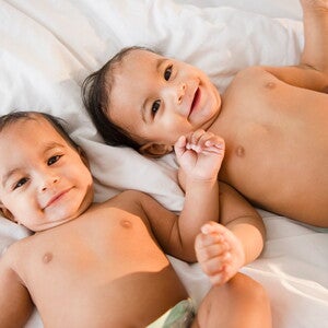 Bebés gemelos o mellizos acostados en una cama sonriendo.