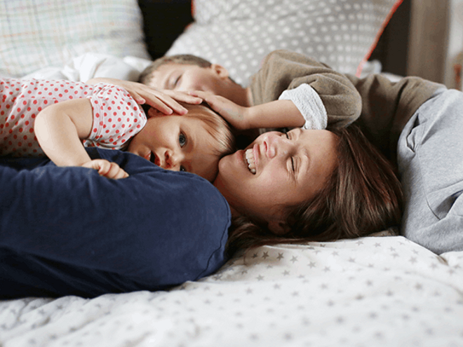 Estrategias efectivas para fomentar la autoestima de tus hijos Una mujer y dos niños felices acostados en una cama.