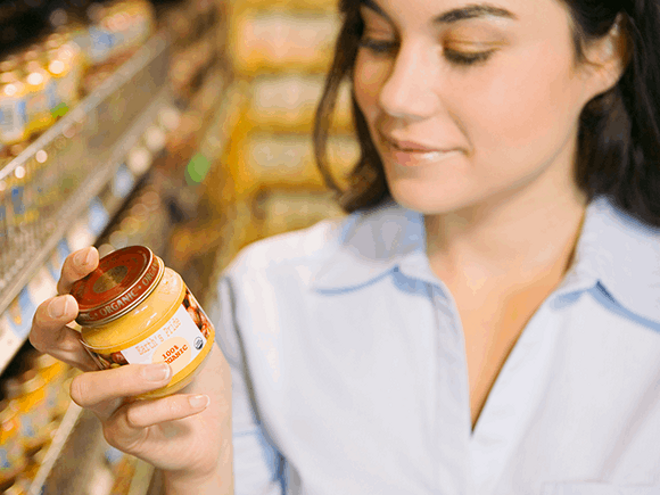 Aprende a leer las etiquetas nutricionales Mujer leyendo etiqueta nutricional con un frasco de colado para bebes