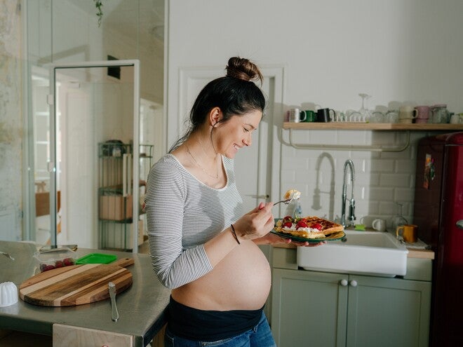 Mujer embarazada sonriendo en la cocina comiendo antojo dulce