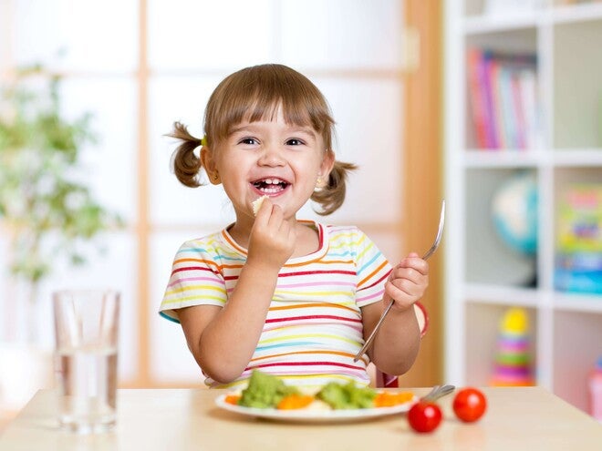 Pequeña comiendo verduras durante la comida.