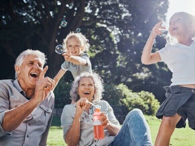Personas adultas mayores y niños jugando al aire libre con burbujas en un parque.