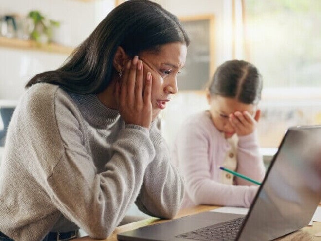 Madre y niña sentadas en la mesa de la cocina con una computadora portátil, realizando una actividad escolar en casa.