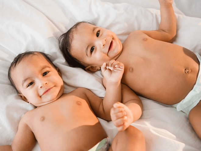 Bebés gemelos o mellizos acostados en una cama sonriendo.