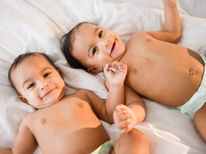 Identifica cuál es la diferencia entre los gemelos y los mellizos. Bebés gemelos sonriendo acostados en la cama.
