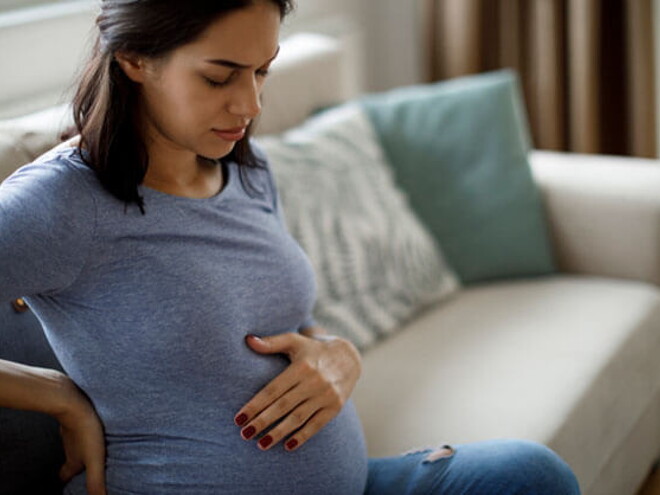 Conoce qué es la eclampsia y cuáles son sus causas. Mamá tocando el vientre y la espalda sintiendo molestia.