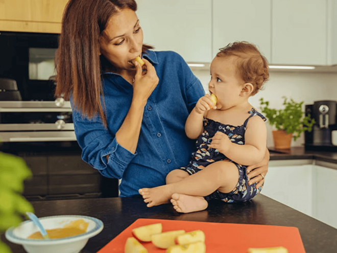 Menú saludable para niños de 12 a 24 meses Mamá y niño pequeño en la cocina comiendo trozos de manzana.