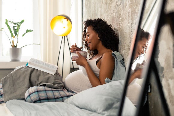 Mujer embarazada sentada en la cama comiendo antojo salado