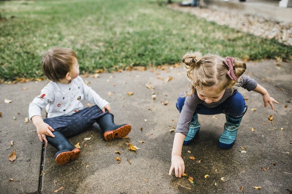 Niño y niña de dos años jugando afuera con hojas de la vereda, actividad para estimular el lenguaje