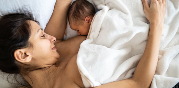 El primer mes, la leche materna pasa por muchos procesos, desde el calostro hasta la leche madura que será la definitiva y el alimento para tu bebé. Mamá acostada alimentando a su bebé recién nacido.