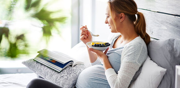 Alimentarse bien es una forma de prevenir la diarrea en el embarazo. Mujer embarazada sentada comiendo frutas.