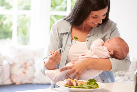 Una madre comiendo con su bebé en brazos Una madre comiendo con su bebé en brazos