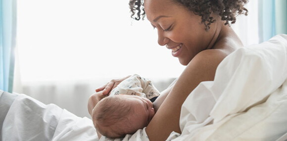 Conoce estos tips para que tengas una lactancia materna exitosa. Mamá acostada alimentando a su bebé recién nacido en la cama.
