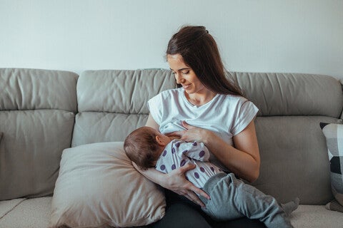 Mamá sentada en un sofá sonriendo, amamantando a su bebé. Lactancia materna.